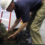A person wearing a hard hat and work clothes is handling a pile of soil or mulch indoors