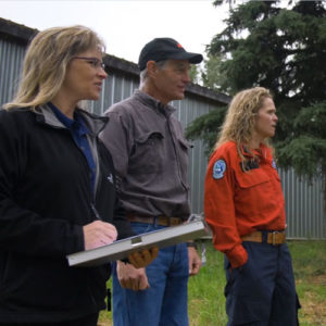 Three people standing outdoors, one holding a clipboard.