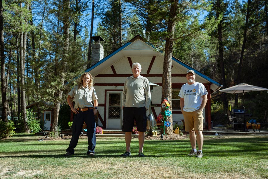 Three people standing in front of a house in a forested area