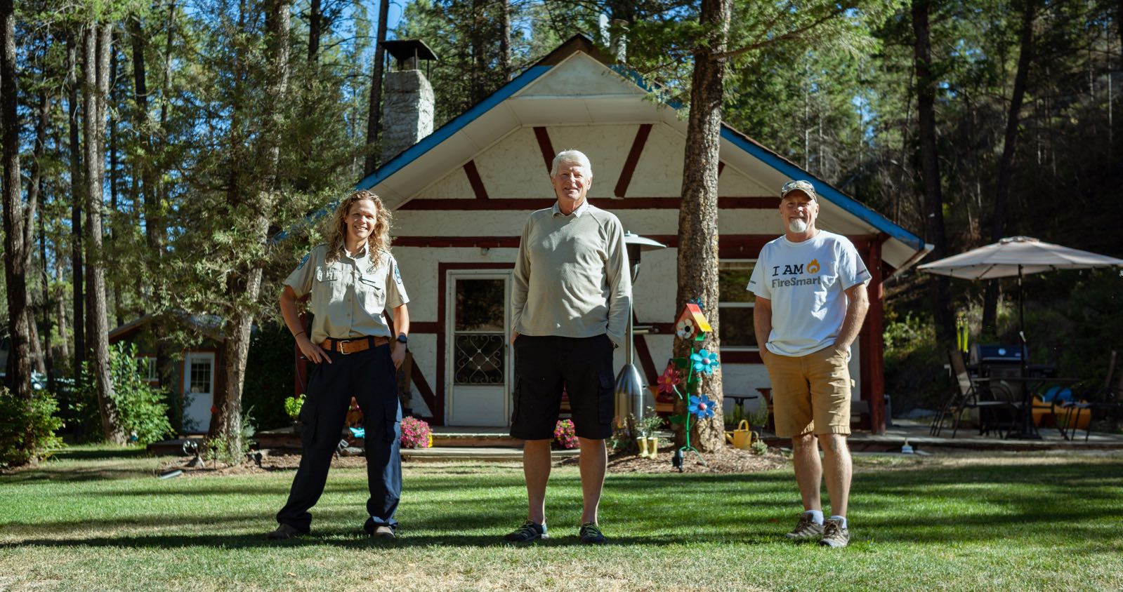 Three people standing in front of a house in a forested area