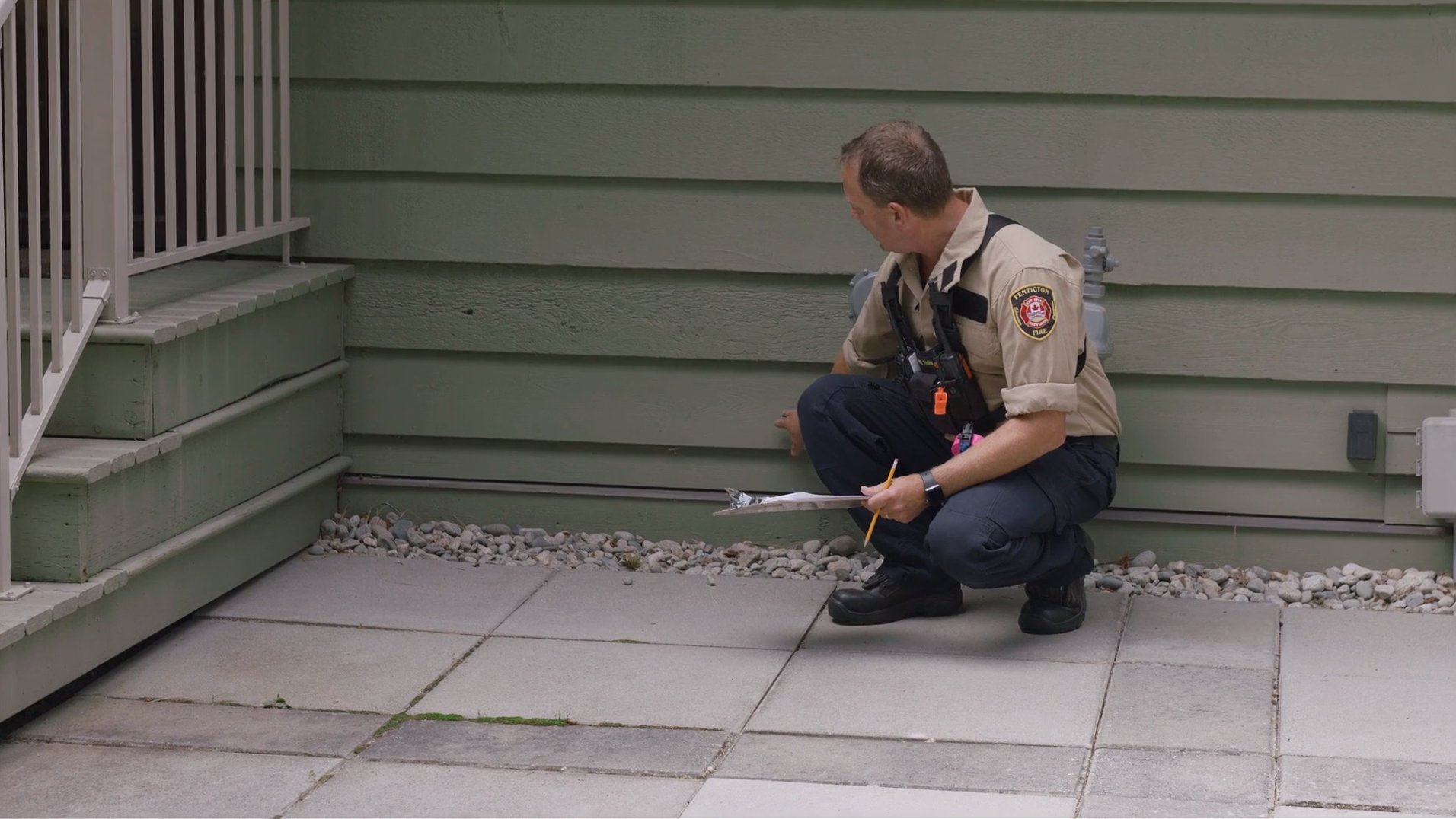 A person in a uniform is kneeling and inspecting the exterior of a house