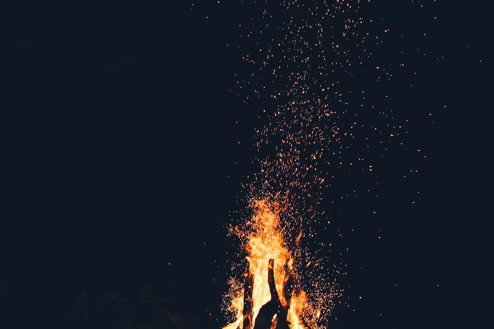 A large fire burning in the dark with sparks rising into the night sky.