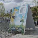 An A-frame sign promoting FireSmart plants stands on a paved area near potted plants.
