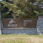 A sign for Whistler with directions to Municipal Hall, Police, and Fire, set between two stone pillars.