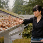 A woman is cleaning leaves and debris from a gutter on a roof.