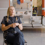 A woman in a uniform is sitting and speaking in a fire station