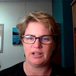 A woman wearing glasses is speaking indoors