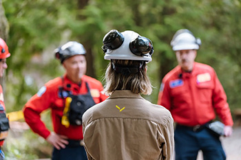 A person wearing a helmet and safety gear faces two other individuals in red uniforms