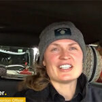 A woman named Kirby Booker is smiling, sitting inside a vehicle, and wearing a beanie.