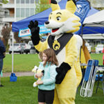 A person in a yellow (firesmart) mascot costume poses with a child holding a toy