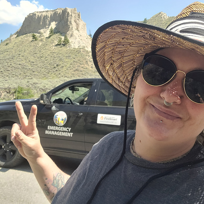 Tammy wearing a wide-brimmed hat and sunglasses is taking a selfie, giving a peace sign.